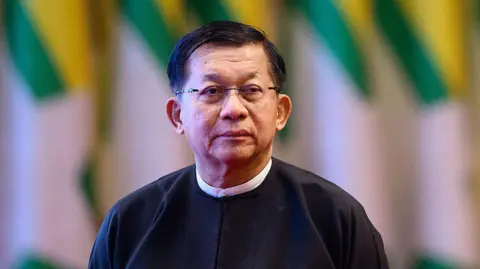 AFP via Getty Images Min Aung Hlaing wears a black top with a white collar and frameless glasses