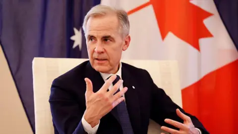 Getty Images Mark Carney, seated and in a suit and tie, gestures as he speaks