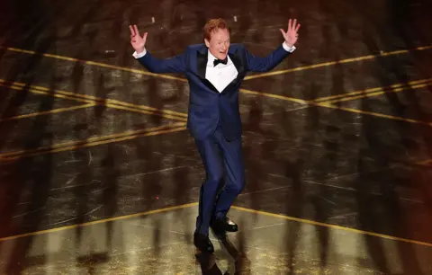 Getty Images Conan O'Brien jumps with his hands in the air while hosting the 98th Academy Awards.