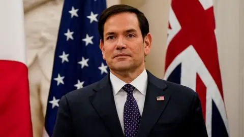 Reuters U.S. Secretary of State Marco Rubio wearing a black suit with a white shirt and a printed tie in Washington in 2025