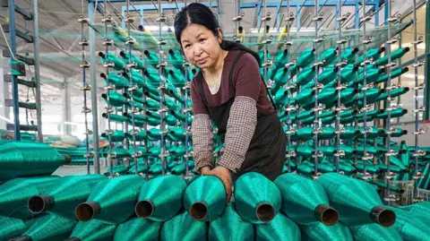 Getty Images A woman stacks rolls of bright green fishing nets on a production line at factory