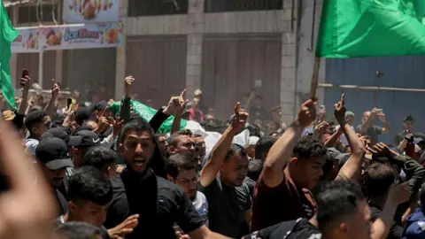 AFP via Getty Images Palestinians carry the bodies of Imad Salim, also known as Abu Hassan, a senior commander in Hamas' armed wing, and others during a funeral procession in Gaza City last month. Men in black are pointing to the sky while some are waving green flags.