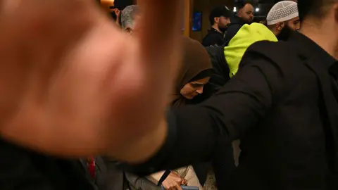 AFP via Getty Images An Australian woman returning from Syrian refugee camps where they have been staying since the Islamic State's demise walks past members of the media as they arrive at the airport in Melbourne