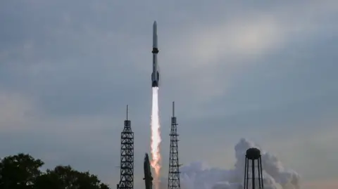 Reuters Blue Origin's New Glenn rocket taking off from a Florida launchpad with a hazy blue sky behind it.