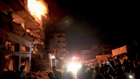Getty Images People look on as a fire burns in a building in central Gaza City.