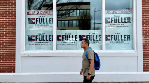 A man walks by Clay Fuller's headquarters, which is plastered with signs that read: Trump endorsed! Clay Fuller Congress. Faith Duty America First.