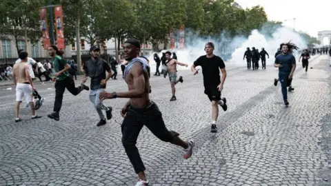 AFP via Getty Images Young men run away from police on a cobbled street. Smoke from tear gas can be seen in the backgound