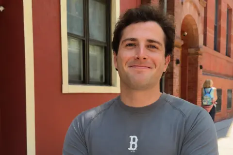 Oliver Zane Picture of Oliver Zane smiling in a grey shirt