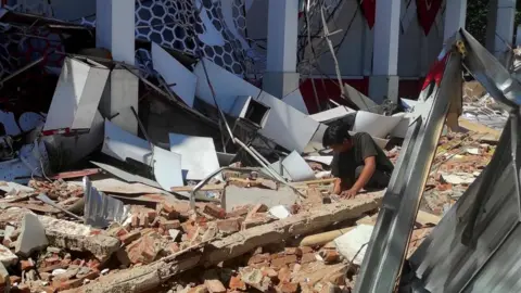 Reuters A resident inspects the damage at a sports complex in Manado