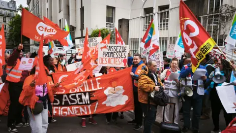 A protest in Paris with demonstrators holding orange flags and placards
