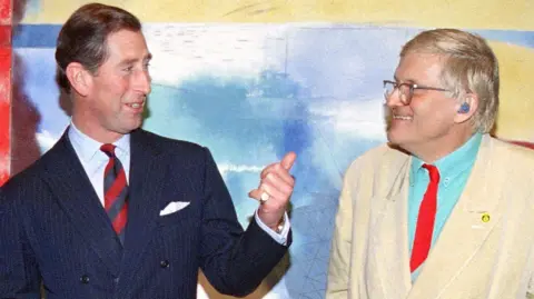 Getty Images The then-Prince of Wales standing next to and speaking to David Hockney in front of one of his brightly-coloured paintings in 1994