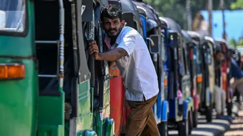 AFP via Getty Images Drivers wait in a queue to refuel their auto rickshaws at a fuel station in Biyagama on the outskirts of Colombo on March 15, 2026.
