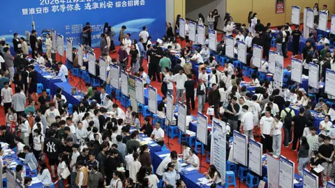 Getty Images Job seekers look at recruitment notices at a job fair targeting college graduates and other job seekers held in the Huai'an University Gymnasium in Huai'an, in China's eastern Jiangsu province on May 22, 2026. 
