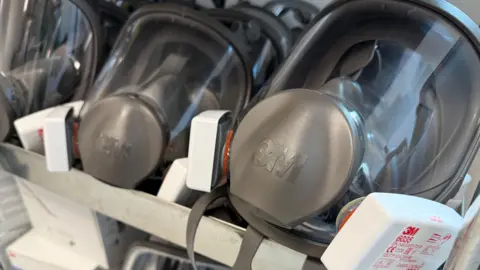 Two grey masks are displayed in a rack with clear panels for the face. 