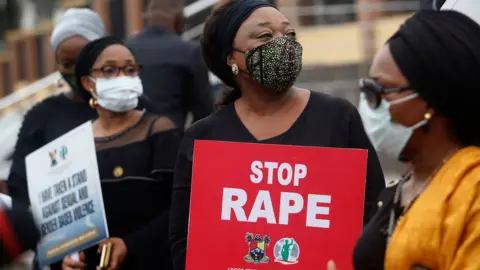 EPA A woman holds a placard saying Stop Rape at a protest in Lagos in 2020. The women are all wearing face masks