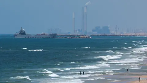 Reuters A ship is pictured off the coast of Gaza near a temporary floating pier anchored to a beach by the US military (16 May 2024)