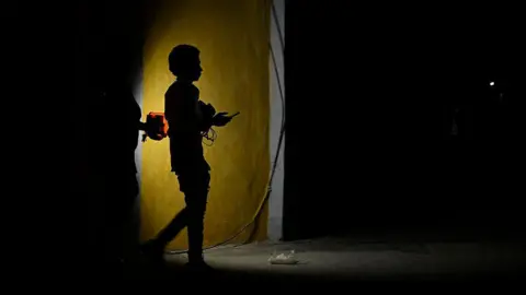 AFP via Getty Images Two people holding a flashlight while walking on a dark street.