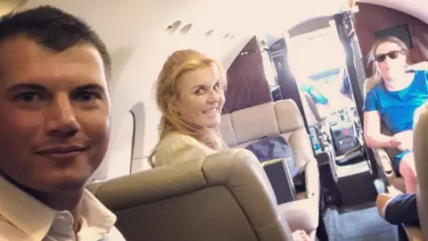 Instagram A social media photo showing Sarah Ferguson smiling at the camera in the centre of the image as she sits in what appears to be a small private jet. In foreground is Michael Evers, a young man with brown hair cropped short and wearing a white shirt, open at the neck.