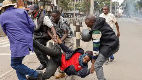 AFP via Getty Images A protester in red shirt, black jacket and black jeans is dragged by four security officers in plain clothes on a street