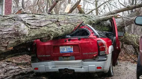 Getty Images A red Chevrolet car is crushed under a large tree that has topped due to a storm