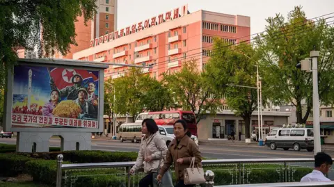 AFP via Getty Images Pedestrians walk past a mural (L) that reads "For the safety and endless future of our nation", as a building adorned with the slogan "Long live the great people-first politics" is seen in the background in Pyongyang on May 8, 2026. 