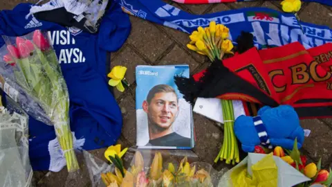 Getty Images Flowers and football tops and scarves on the ground, surrounding a photograph of a young man, on the front of a magazine entitled 