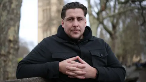 Getty Images A man looks straight at the camera. He is wearing a black coat. The framing and content of the picture look sombre.