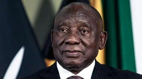 Getty Images A head-and-shoulders image of Cyril Ramaphosa. He is wearing a dark suit and the white collar of his shirt can just be seen. Some flags are out of focus in the background.