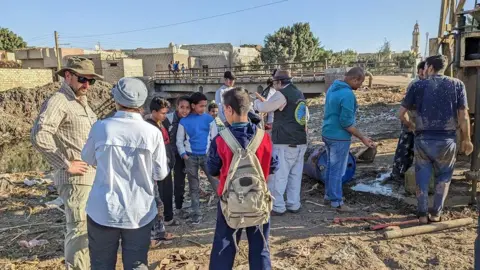 Suzanne Onstine Researchers stand among children at an archaeological site in Egypt