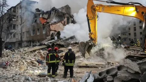 Reuters A digger moves debris as emergency service personnel watch on and douse flames from an apartment block fire in Kharkiv