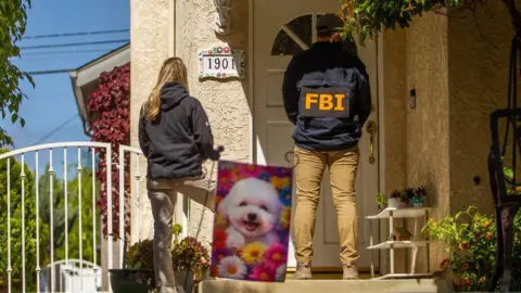 Getty Images A man with an 'FBI' jacket and a woman in a hooded top have their backs to us as they stand facing the front door of a house. FBI agents are canvassing the neighbourhood of the suspected press dinner gunman
