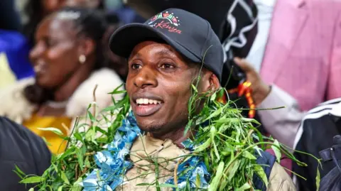 EPA Kenyan World Marathon Record holder Sabastian Sawe smiles with wreaths laid around his neck.