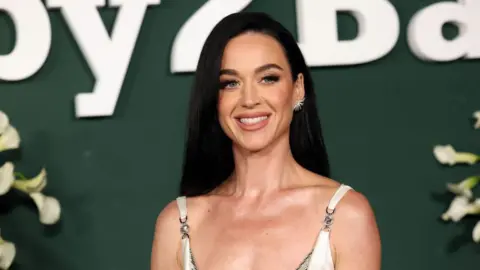 Getty Images Close-up shot of pop star Katy Perry in a white dress, wearing her long black hair down, against a dark green background