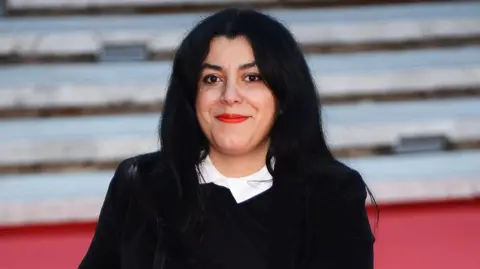 Getty Images Marjane Satrapi smiling at the camera while wearing a black jacket