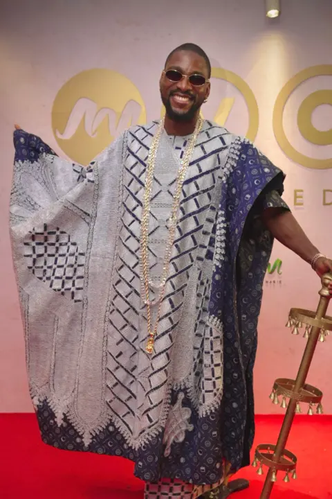 BBC/GIFT UFUOMA Tobi Bakre is dressed in a traditional outfit and is carrying a brass staff