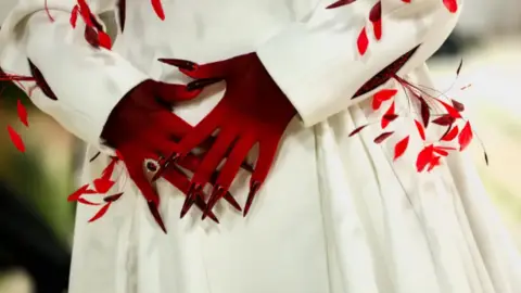 REUTERS/Daniel Cole Naomi Osaka's hands are seen close up in red gloves with long nails against a full white skirt