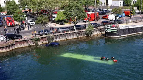 Reuters The River Seine in Juvisy-sur-Orge. The roof of a bus can be seen under the water, on which a small group of people are sitting. On the road nearby there are police cars and fire engines.