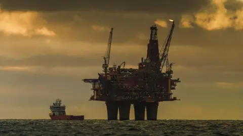 Getty Images An oil rig in the North Sea on a cloudy day in the evening with a ship to the left of it.