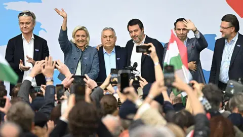 AFP via Getty Images A woman joins Viktor Orban and other men on stage in front of a crowd of photographers
