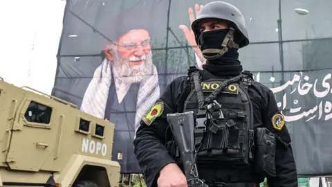 AFP A member of the Iranian security forces stands guard next to a banner honouring the assassinated Supreme Leader, Ayatollah Ali Khamenei, in Tehran, Iran (31 March 2026)