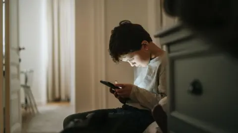 Getty Images A boy stares down at a phone screen
