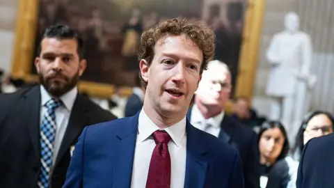 Getty Images Mark Zuckerberg wearing a blue suit and red tie, walking through the Capitol. 