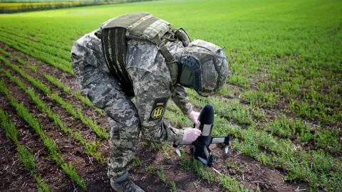 Lee Durant/BBC A Ukrainian soldier in uniform sets up an interceptor drone in a field