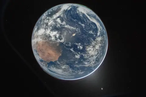 Nasa/Reid Wiseman A picture of the Earth from space, which centres the planet against the dark background of space. It's a round blue planet. Clouds can be seen and a thin green aurora at the top.