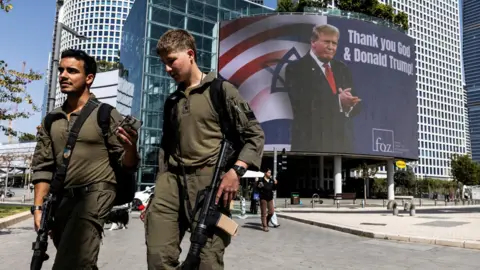 Reuters Israeli soldiers walk by a billboard commissioned by an evangelical group, which displays a picture of US President Donald Trump with the words "Thank you God & Donald Trump", in Tel Aviv, Israel (12 March 2026)