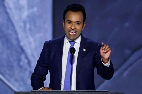 Getty Images Vivek Ramaswamy stands at a lecturn and gestures as he speaks.