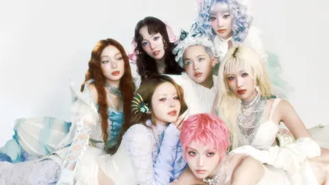 XGALX The seven members of XG pose for a promotional photo in a triangular formation, weaing a variety of pastel shaded, Victorian-inspired outfits