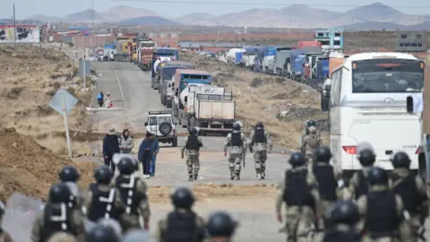 Reuters Riot police walk along a road lined with trucks held up by a roadblock in Bolivia