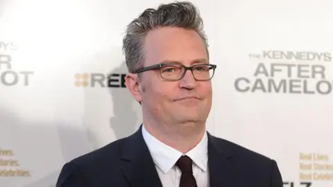 Jason LaVeris/FilmMagic via Getty Images Matthew Perry wears glasses and a dark suit. He is posing for a picture on an event red carpet.