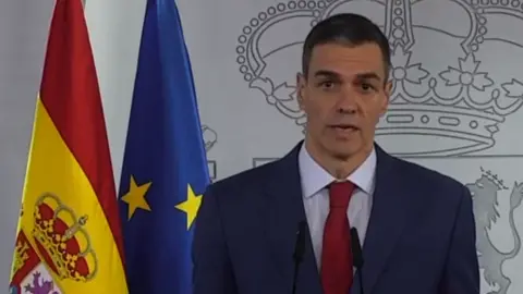 La Moncloa A man in a suit and tie standing next to a yellow and blue flag